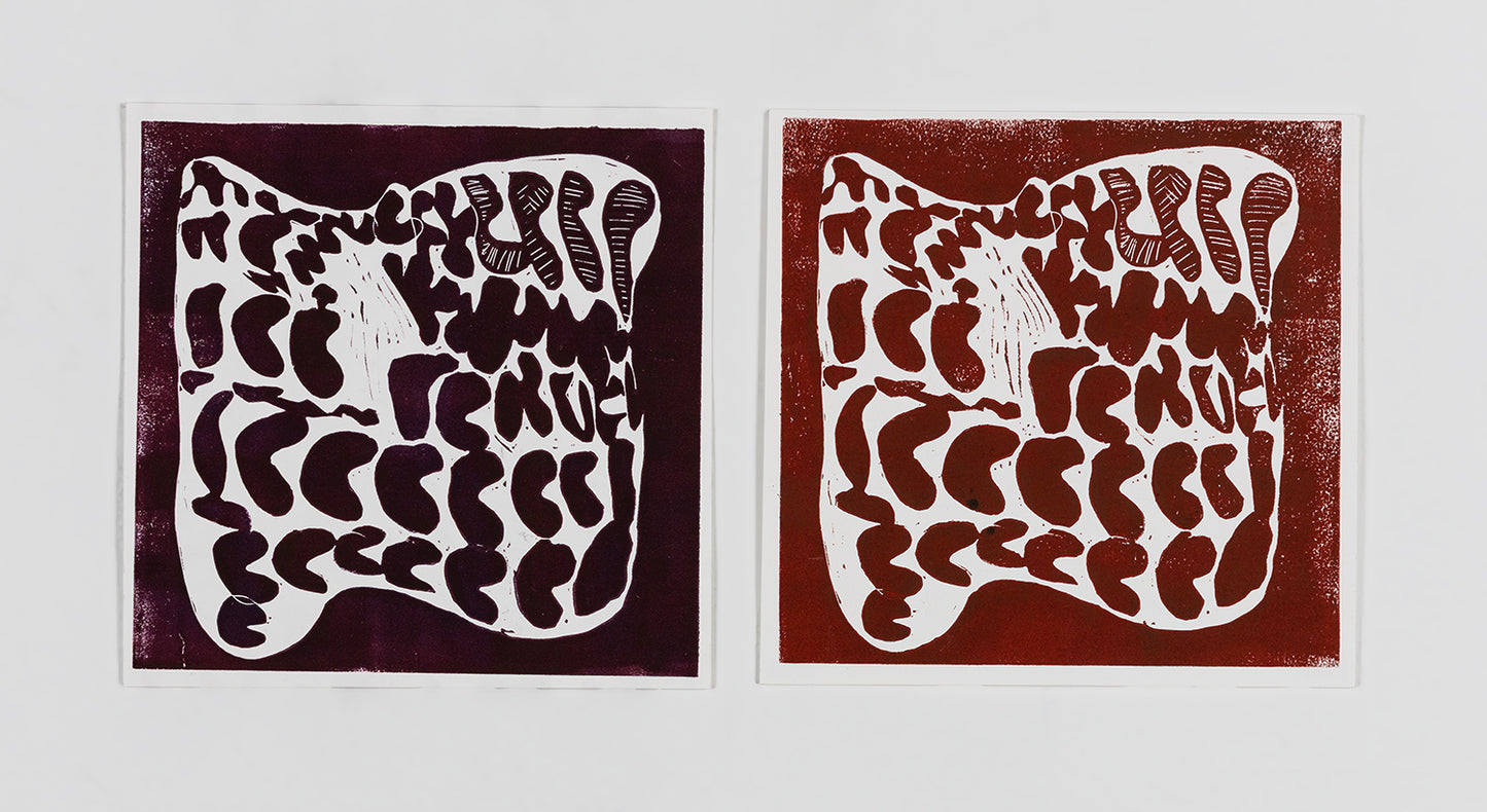 Two abstract linoblock prints on square pieces of paper, arranged side by side. The image on each print is the same: rows of symbols, each shaped like a bean or bubble letter, are crowded together inside a larger white shape. The print on the left is dark reddish brown, and the print on the right is a lighter brown ink.
