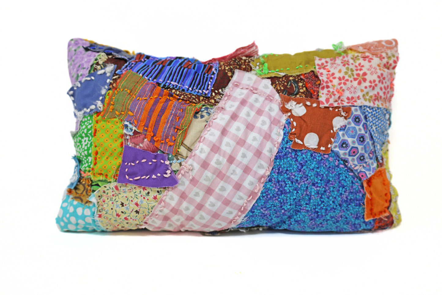 This fiber pillow incorporates various patterns and materials to form a patchwork style. It has vibrant colors and patterns, with many of the fabrics containing floral and striped elements. There are also embroidered details.