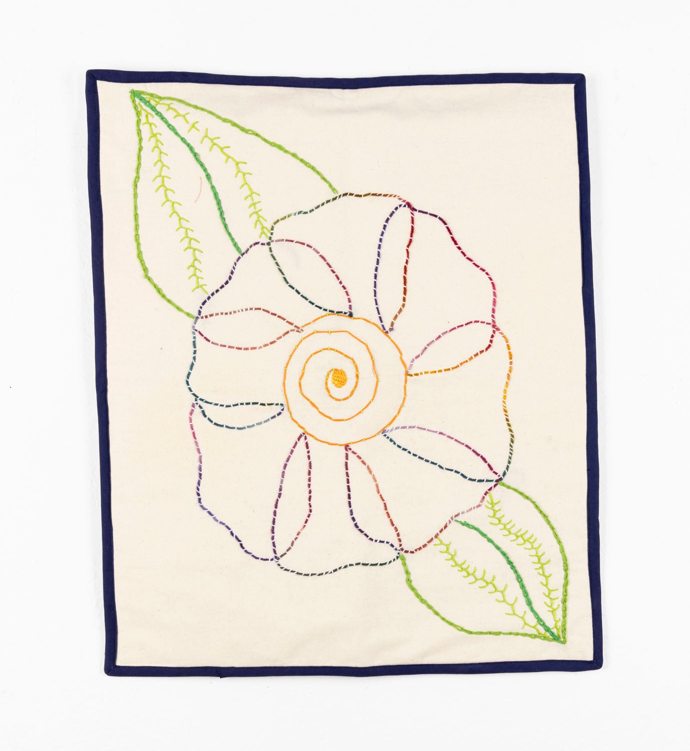 This fiber piece has a large flower embroidered onto fabric. The middle of the flower is a vibrant yellow thread, with blue, pink and purple petals. The leaves are varying shades of green. The flower is depicted through a strong sense of line-work against the beige background.