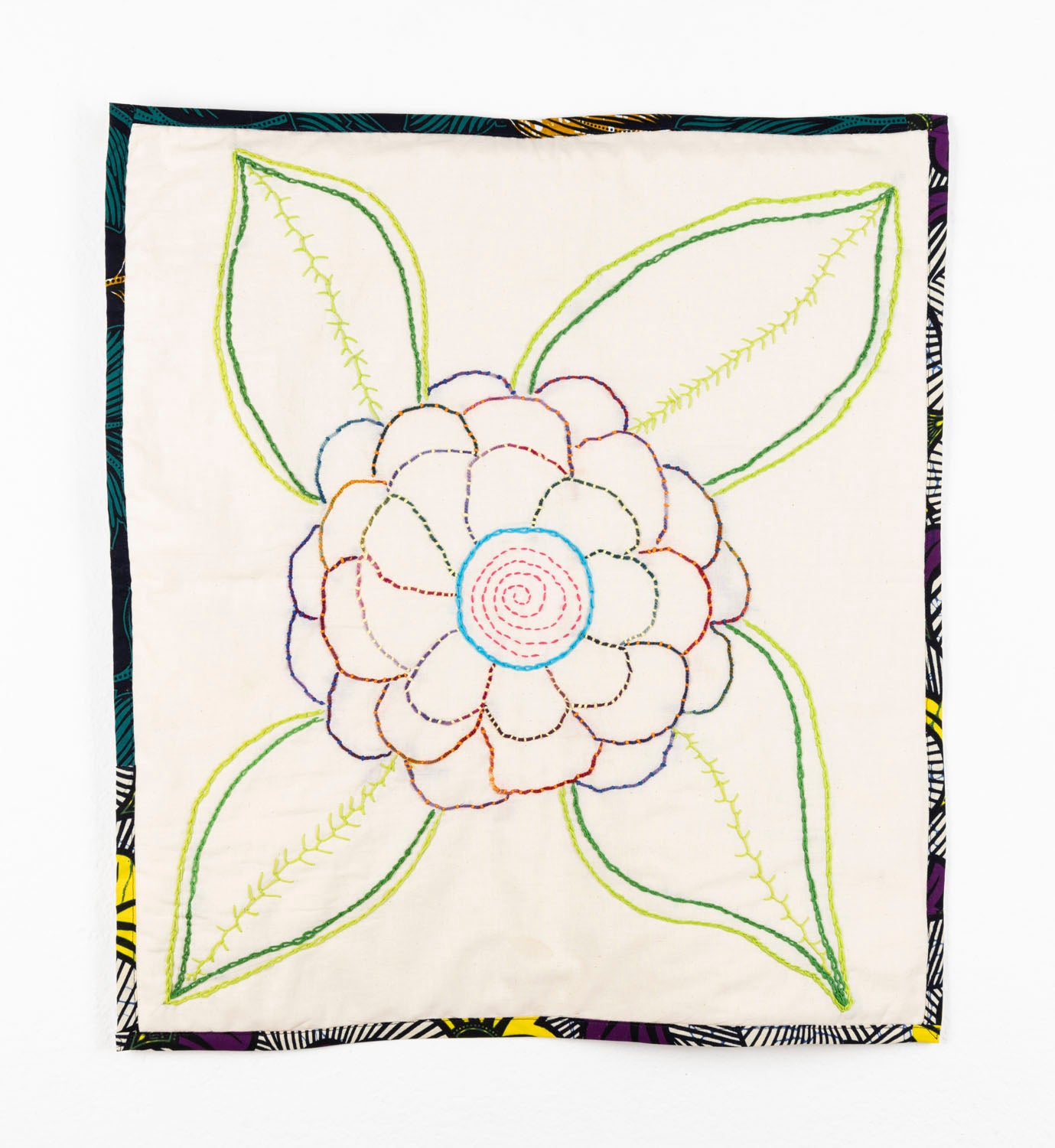 This fiber piece has a large flower embroidered onto fabric. The middle of the flower is a vibrant blue and pink thread, with purple, green, orange and red petals. The leaves are varying shades of green. The flower is depicted through a strong sense of line-work against the beige background. The piece also has a floral fabric background.