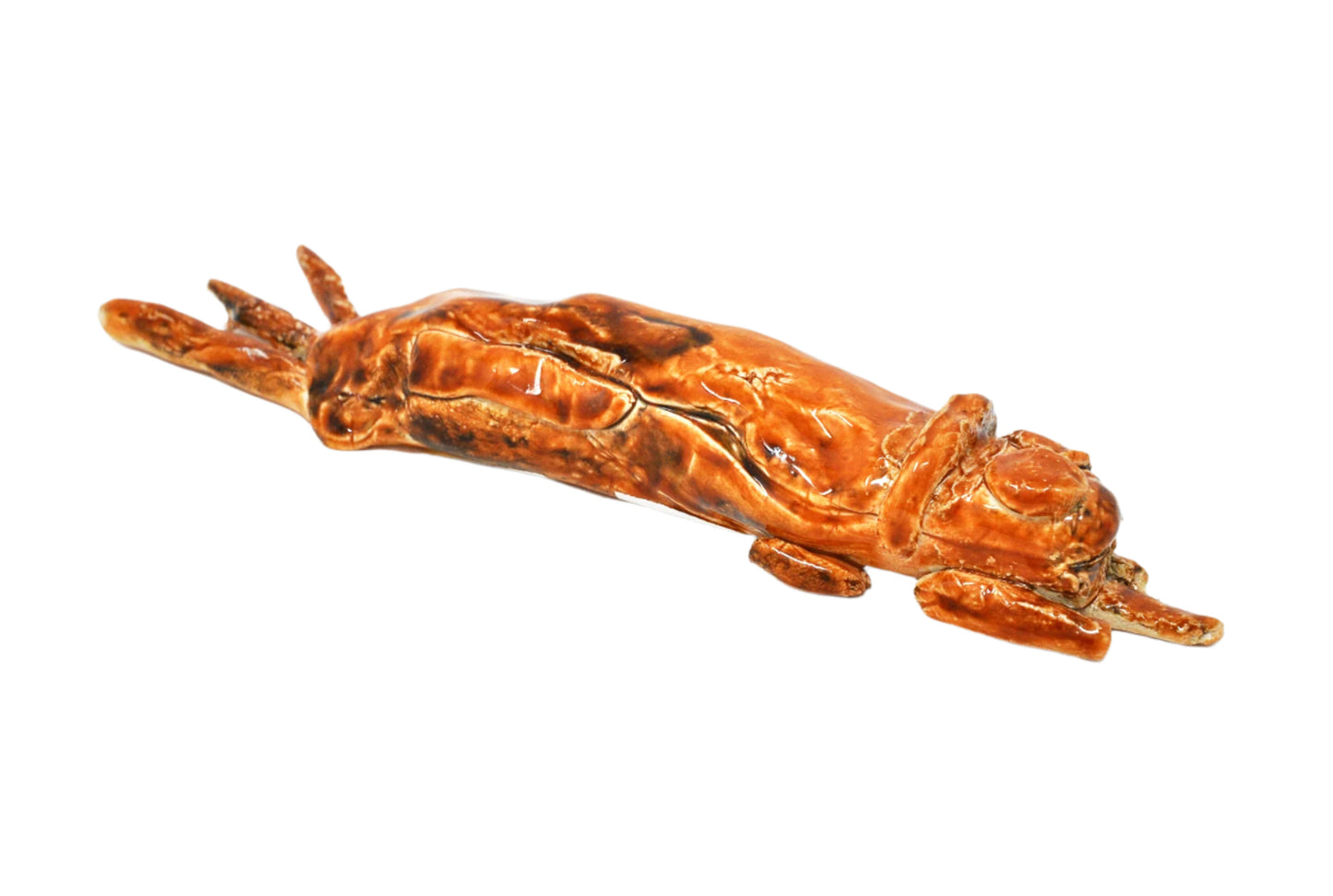 A small ceramic sculpture of an abstracted dog, glazed all over in dark caramel brown. The dog is a long cylindrical form with thinner rolled tubes sticking out around the sides. The dog is sculpted in a prone/lying down position, with its legs and tail sticking out from one end, and its arms, ears, and tongue sticking out from the other.