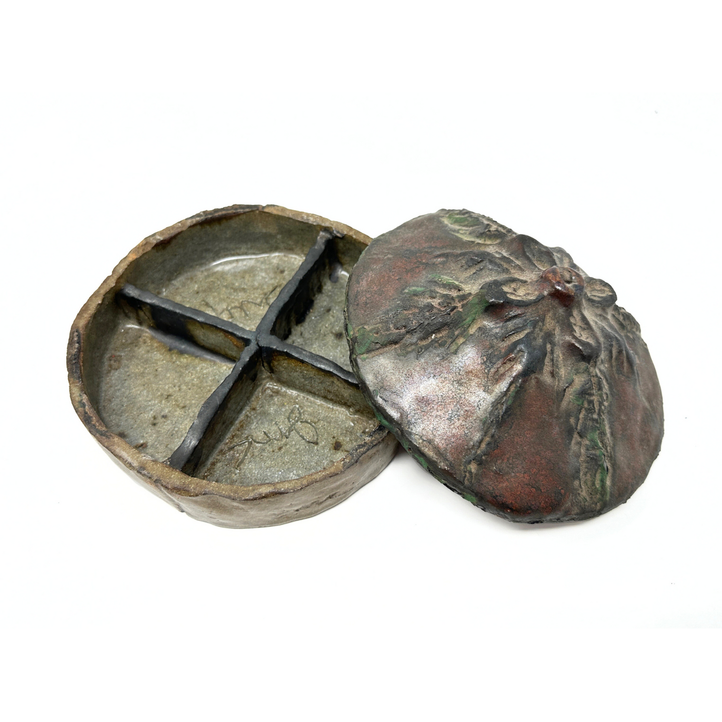 The same container, photographed with the lid off and lying next to the base. The interior of the container is divided into 4 sections by 4 slabs that cross at the center. The artist has etched their initials on the interior base of the container.