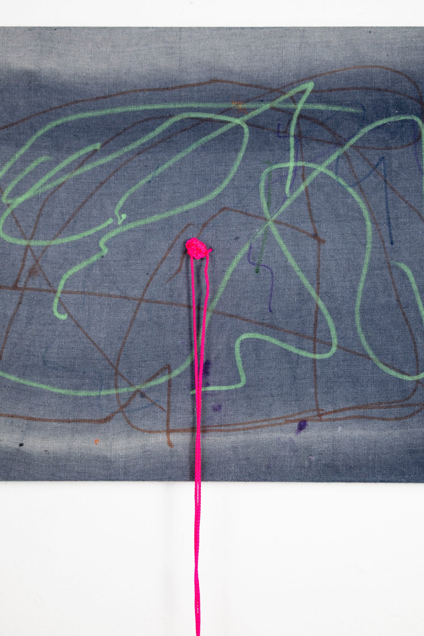 A rectangle artwork on stretched gray fabric that has been sun bleached. There are green and burgundy acrylic marker squiggle lines throughout. In the middle of the artwork, a neon pink string has been knotted and strung through, and hangs loose a few inches below the artwork.