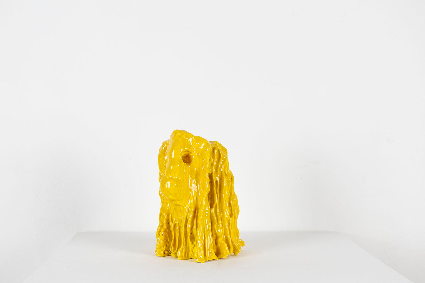Yellow ceramic dog sculpture on a white background, photographed in profile