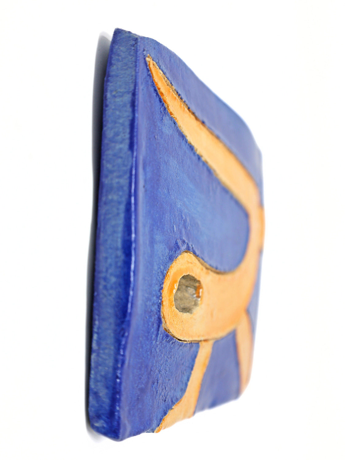 This ceramic piece is a stylized depiction of a sea snake. The sea snake is glazed in a bright orange which complements the dark blue background. The sea snake is carved out from the piece.