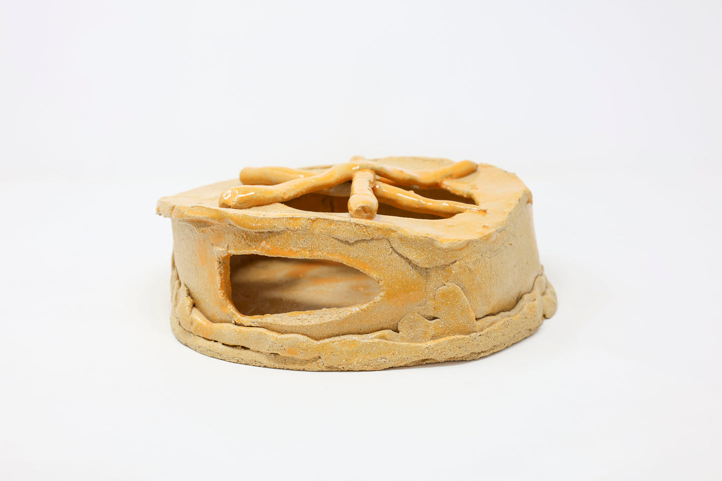 Yellow hollow ceramic sculpture with a naturalistic design. It is a cylindrical vessel with an opening at the front and partial openings at the top.