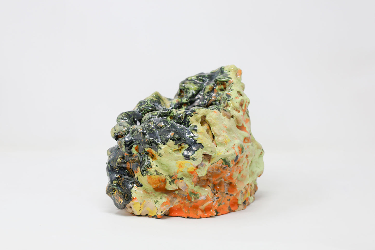 Abstract hollow ceramic sculpture, lumpy in form and glossy in texture, colored with green, orange and black glaze.
