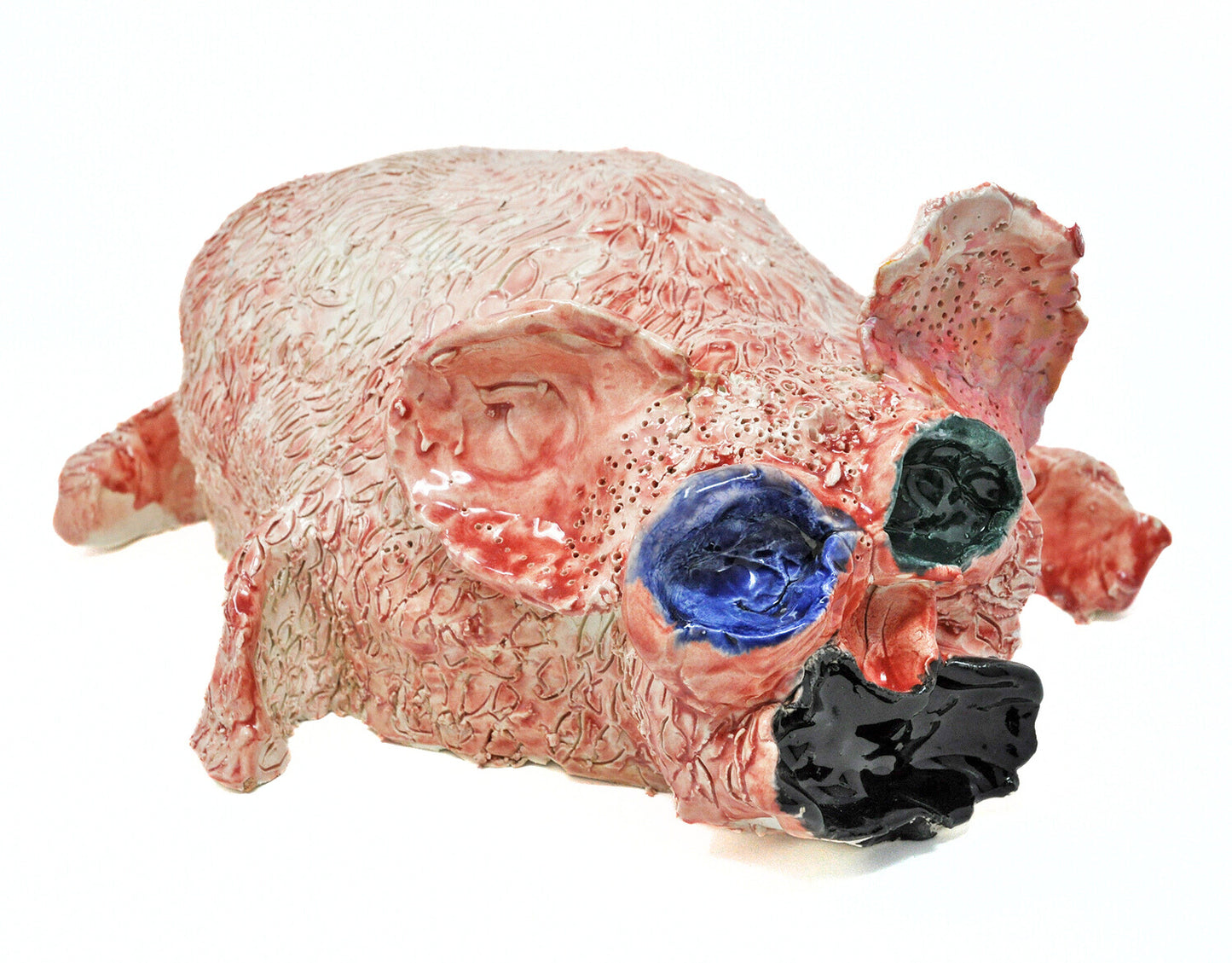 a ceramic sculpture of a small pink animal, similar to a rabbit or a piglet, with round ears blue and black eyes, and a wide open black mouth. The surface of the sculpture is textured all over with etched dots and lines.