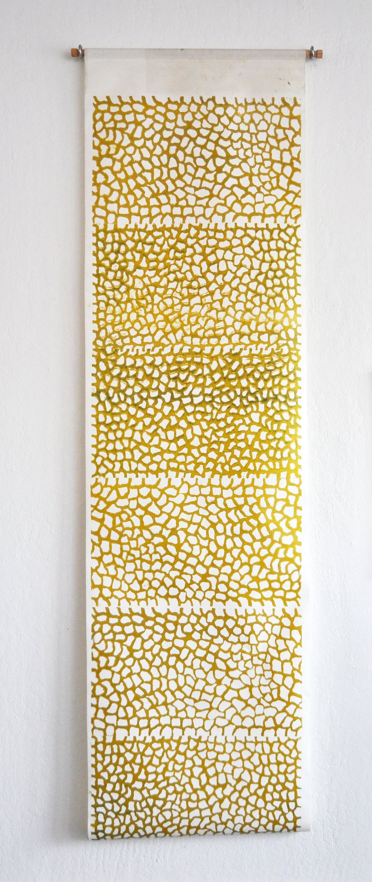 A vertical linocut print featuring a geometric pattern of gold and white dots on a yellow background, presented on a wooden dowel.