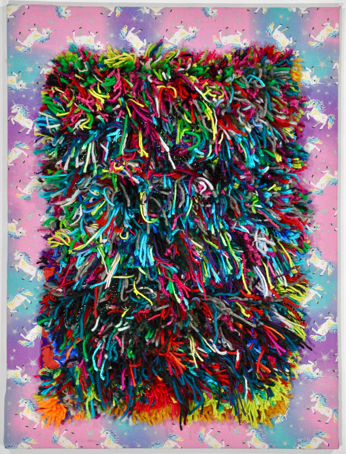 A fiber piece featuring tufted yarn on stretched fabric with a colorful, fuzzy appearance on a pink background with a unicorn pattern.