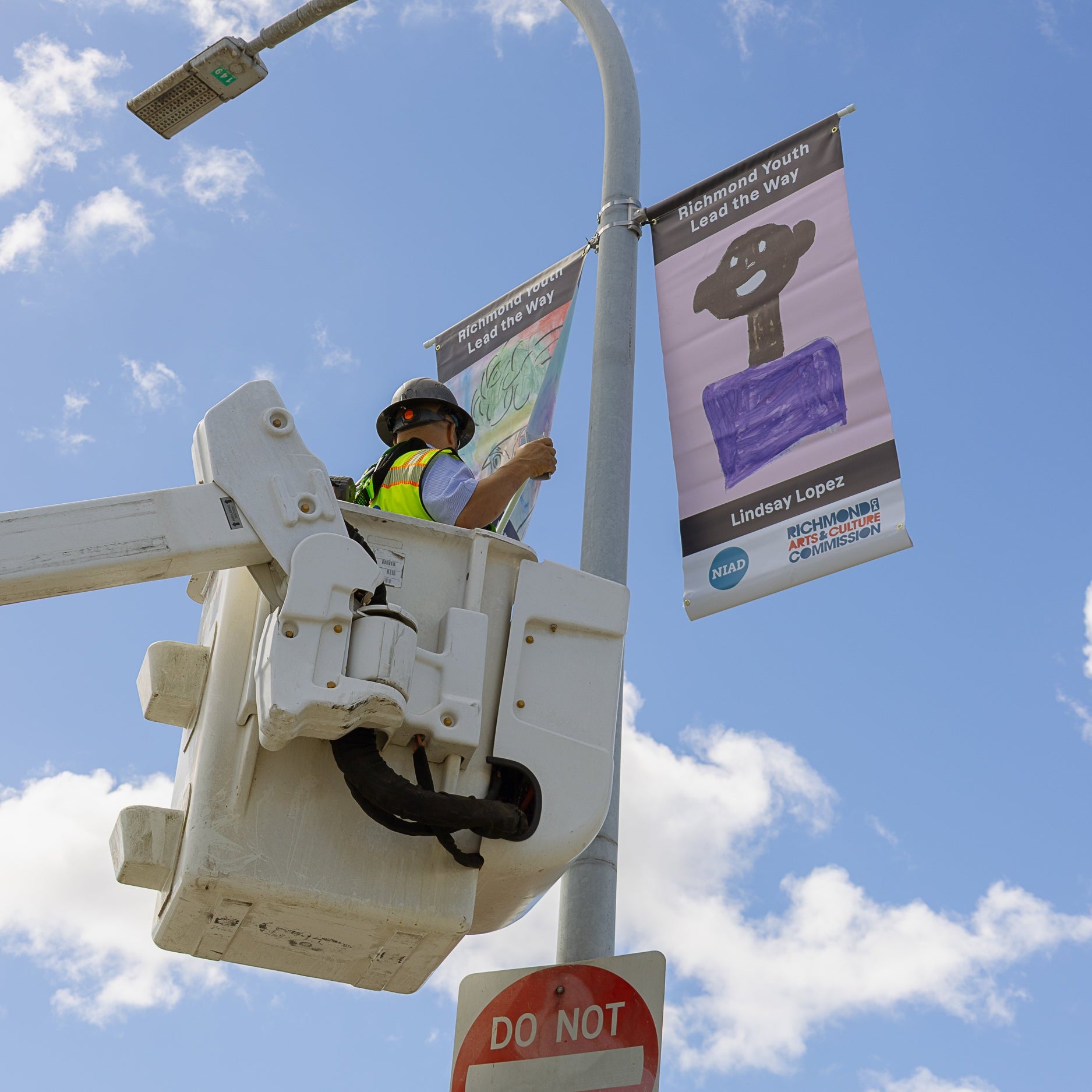 person installing banners on light pole with blue sky and clouds in background