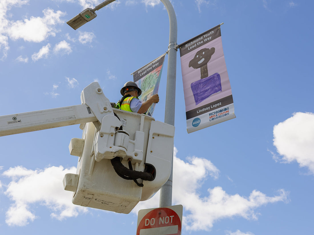 person installing banners on light pole with blue sky and clouds in background