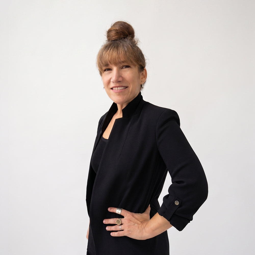Headshot of Amy Kisch, a woman with light brown hair pulled back, smiling, wearing a black jacket, standing against a plain light gray background.