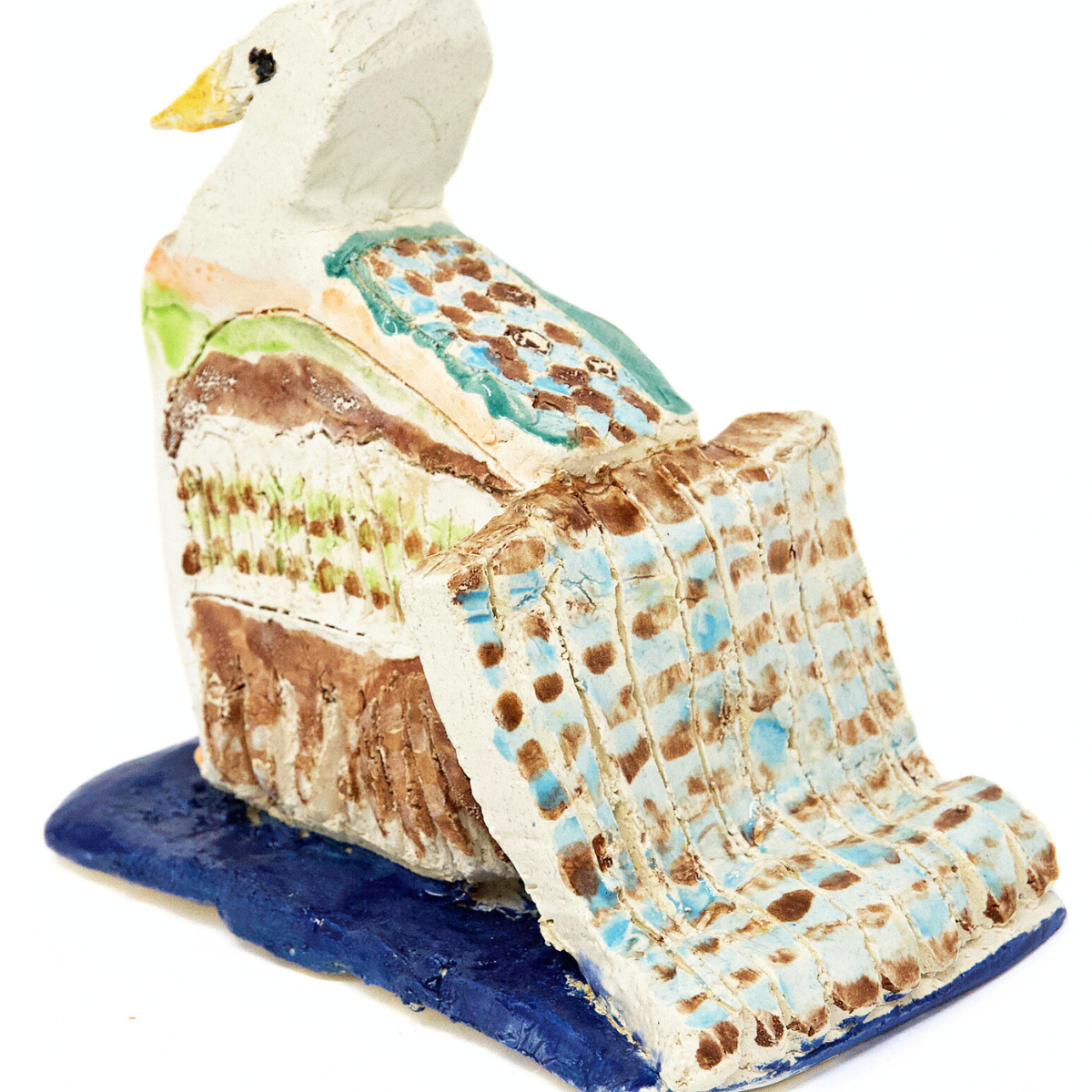 a small ceramic sculpture of a multi-colored bird. The bird is glazed in blue, brown, and green spots. It’s positioned like it’s swimming away: it has a long spotted tail and sits on a blue glazed ceramic square.