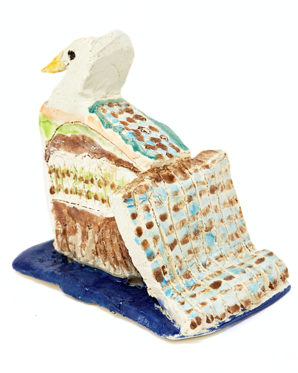 a small ceramic sculpture of a multi-colored bird. The bird is glazed in blue, brown, and green spots. It’s positioned like it’s swimming away: it has a long spotted tail and sits on a blue glazed ceramic square.