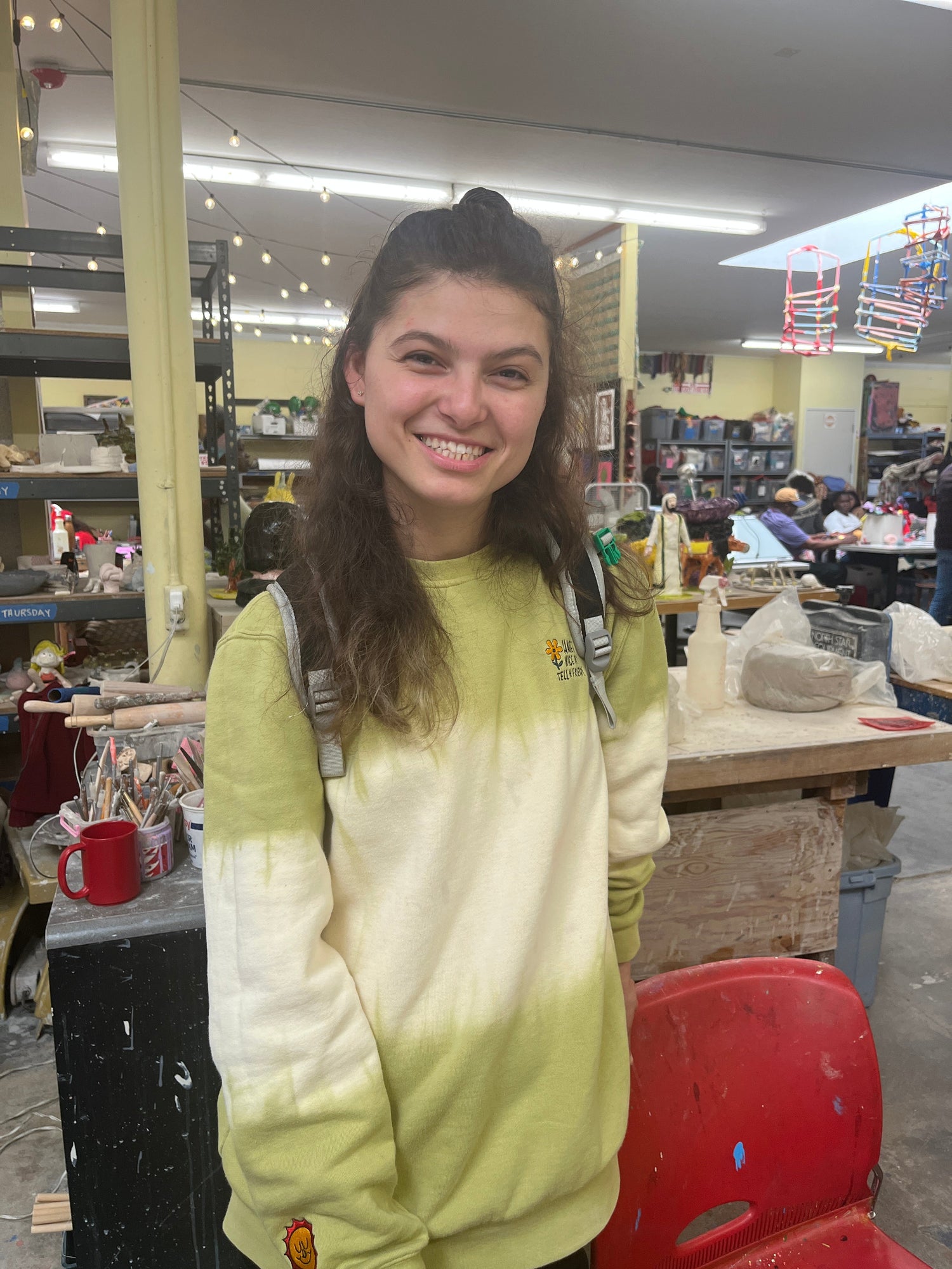 A photo portrait of a light skinned young woman, standing and smiling with long brown hair and a green and white sweater