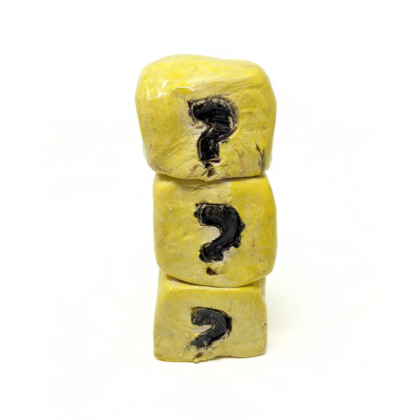 A small ceramic sculpture of three hand-built yellow cubes in a stack. Each cube has a question mark etched on its surface and painted black. This object references the mystery boxes from the video game Super Mario