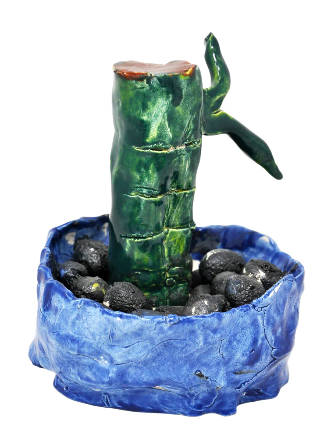 A small ceramic sculpture of a green bamboo shoot growing in a blue container. Round black ceramic pebbles are arranged around the base of the bamboo.