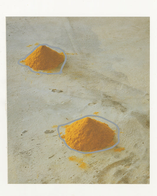 A photograph of two piles of yellow powder on a textured beige surface with silver outlines drawn around the mounds. 