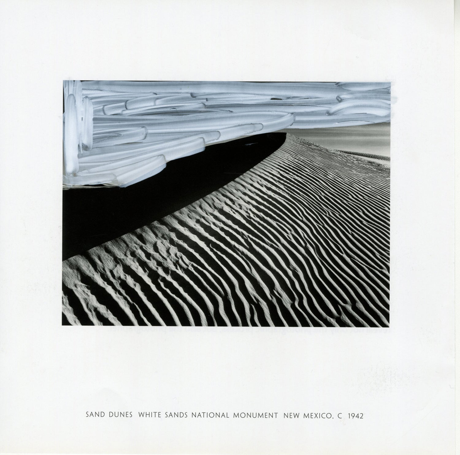 A black and white photograph by Ansel Adams capturing the rippling patterns of sand dunes at White Sands National Monument, New Mexico, dated around 1942. The foreground features intricate, parallel lines formed by the wind's effect on the sand, creating a texture of shadows and highlights. In the upper portion, there are modifications with white acrylic marker, adding broad strokes that contrast with the natural patterns of the sand. 