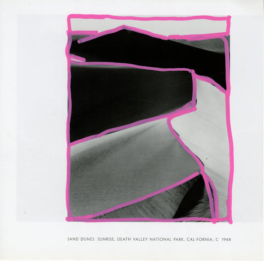 A black-and-white photograph by Ansel Adams depicting sand dunes at sunrise, located in Death Valley National Park, California. The foreground shows smooth, undulating dunes with intricate patterns of light and shadow, creating a contrast. The upper section reveals the horizon with the dark silhouette of distant dunes or mountains against the sky. On the printed photo are pink acrylic marker lines that trace irregular shapes following the contours of the dunes and edges, creating a dynamic visual overlay.
