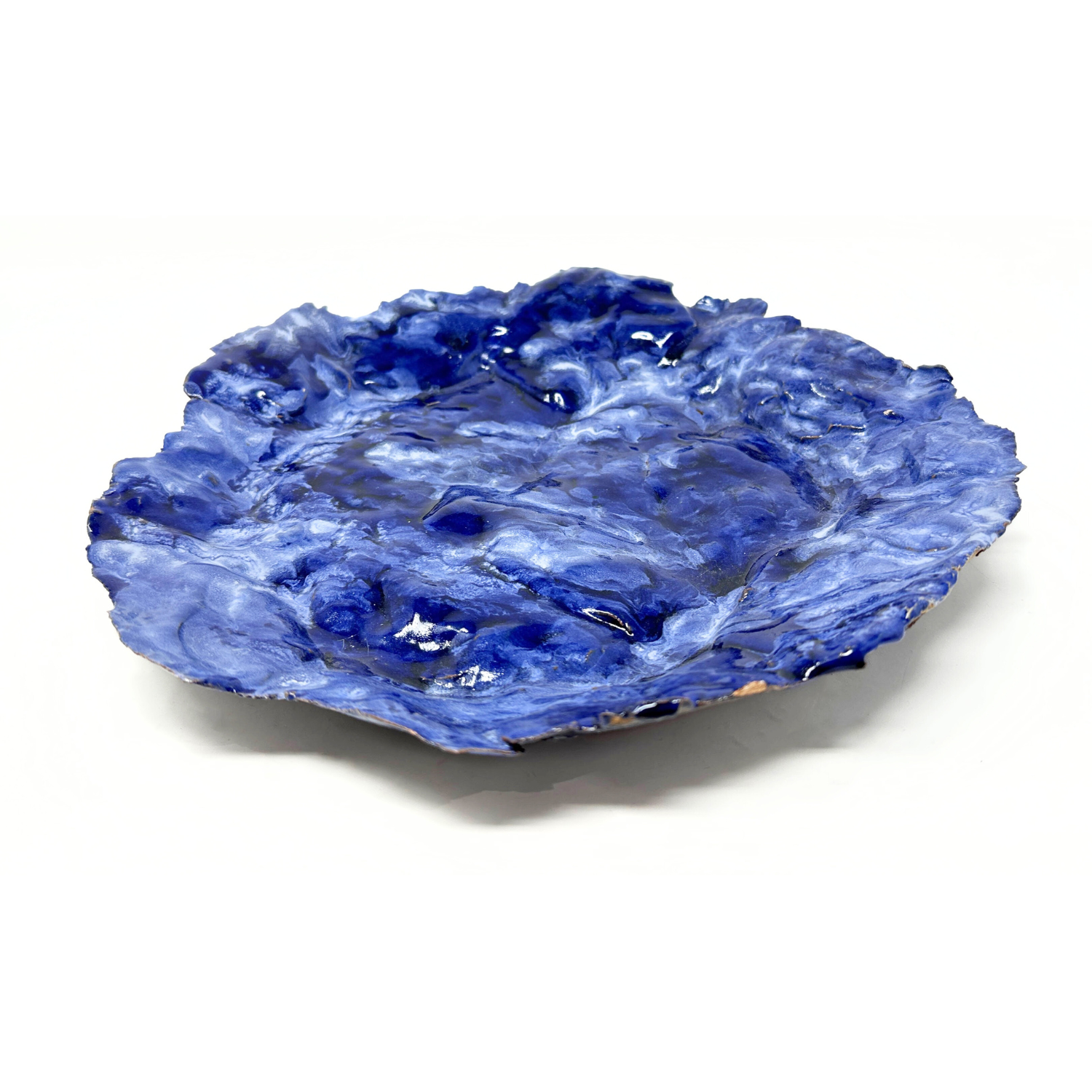 A hand built ceramic plate, glazed all over in glossy mottled blues. The edges of the plate are delicately ruffled like the edges of rose petals. 