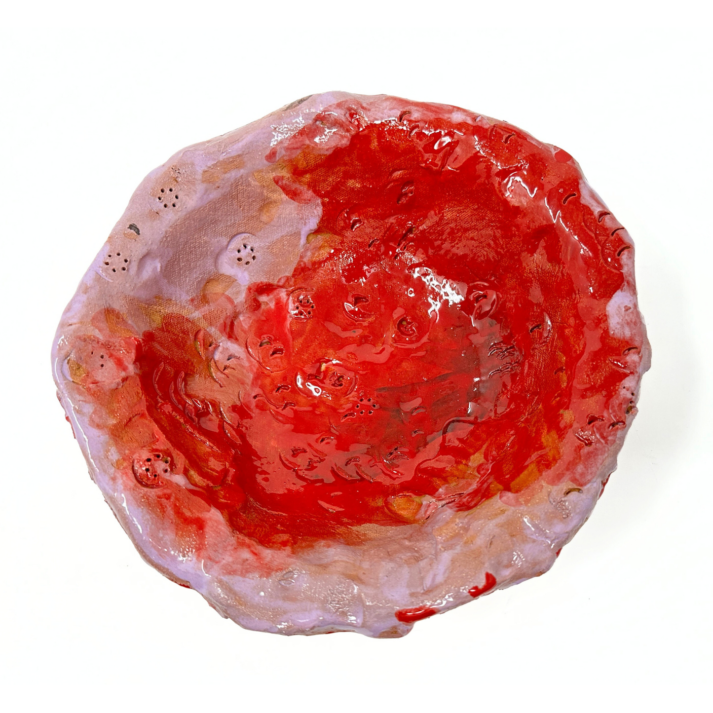 A ceramic bowl photographed from above to show the interior surface. The bowl is glazed mostly with bright red with pale pink areas around the rim. There are multiple imprints of round buttons pressed into the surface of the bowl. The edge of the bowl is lumpy and the glaze has been applied thickly. 