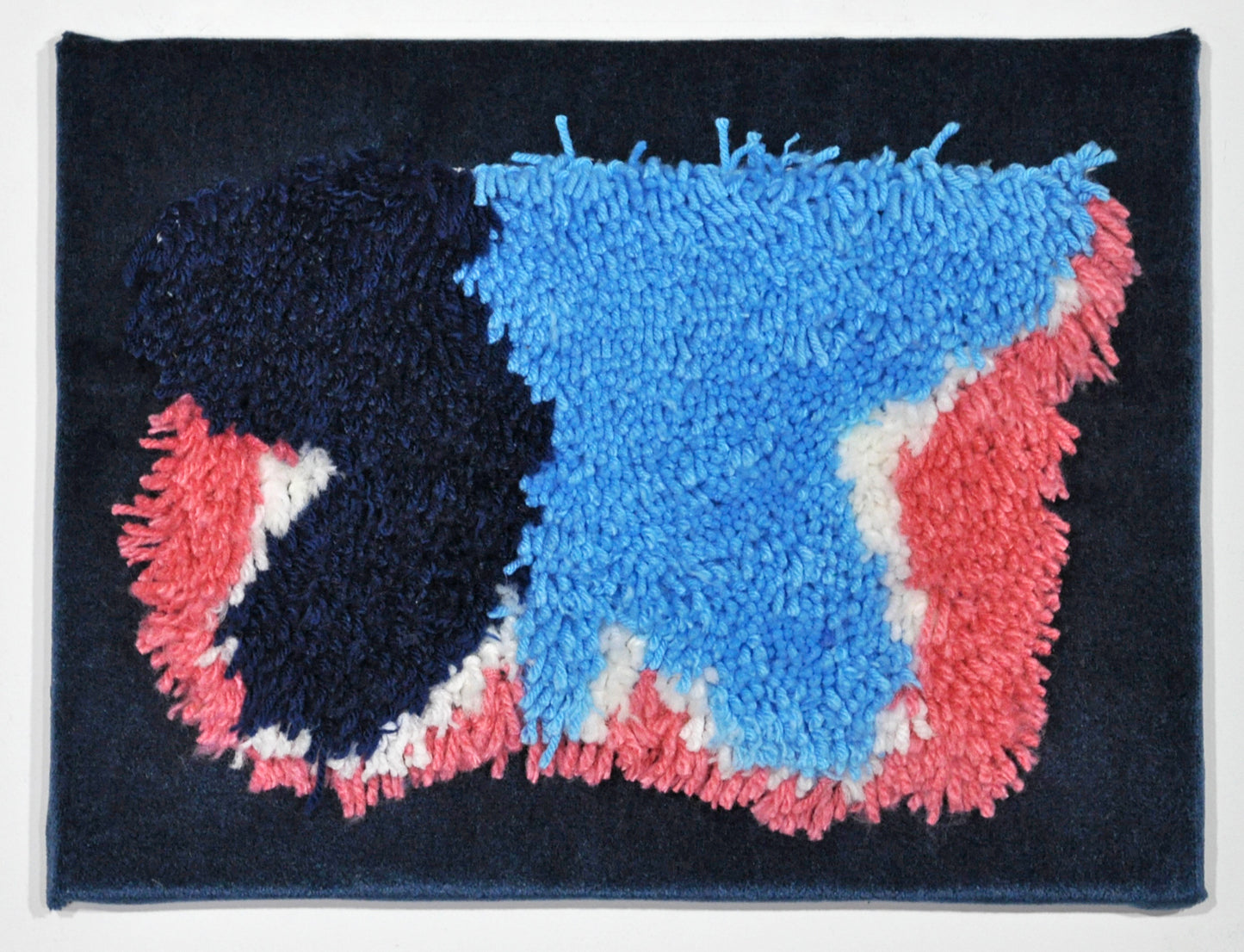 A tufted yarn shape on a blue velvet rectangle. The shape is reminiscent of a butterfly, and is comprised of pink, white, navy, and light blue yarn.