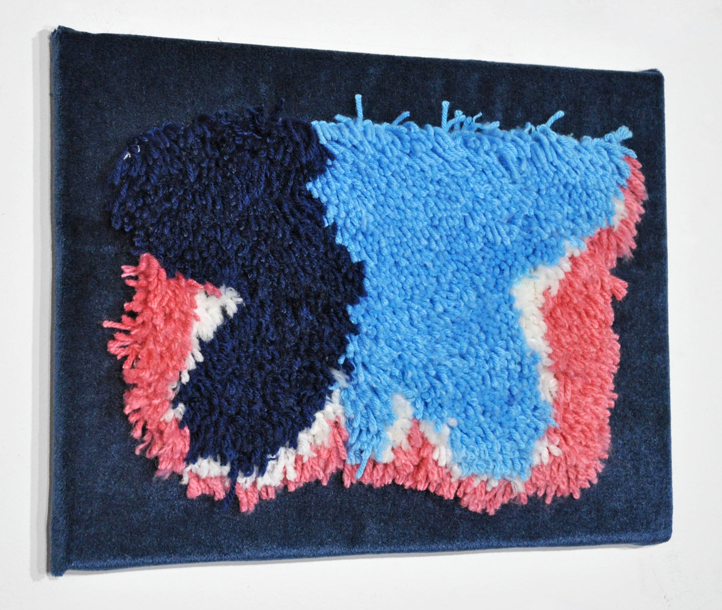 the same artwork photographed from a slight angle to show the dimension of the work. the tufted pieces of yarn extend out half an inch further than the blue velvet backing.