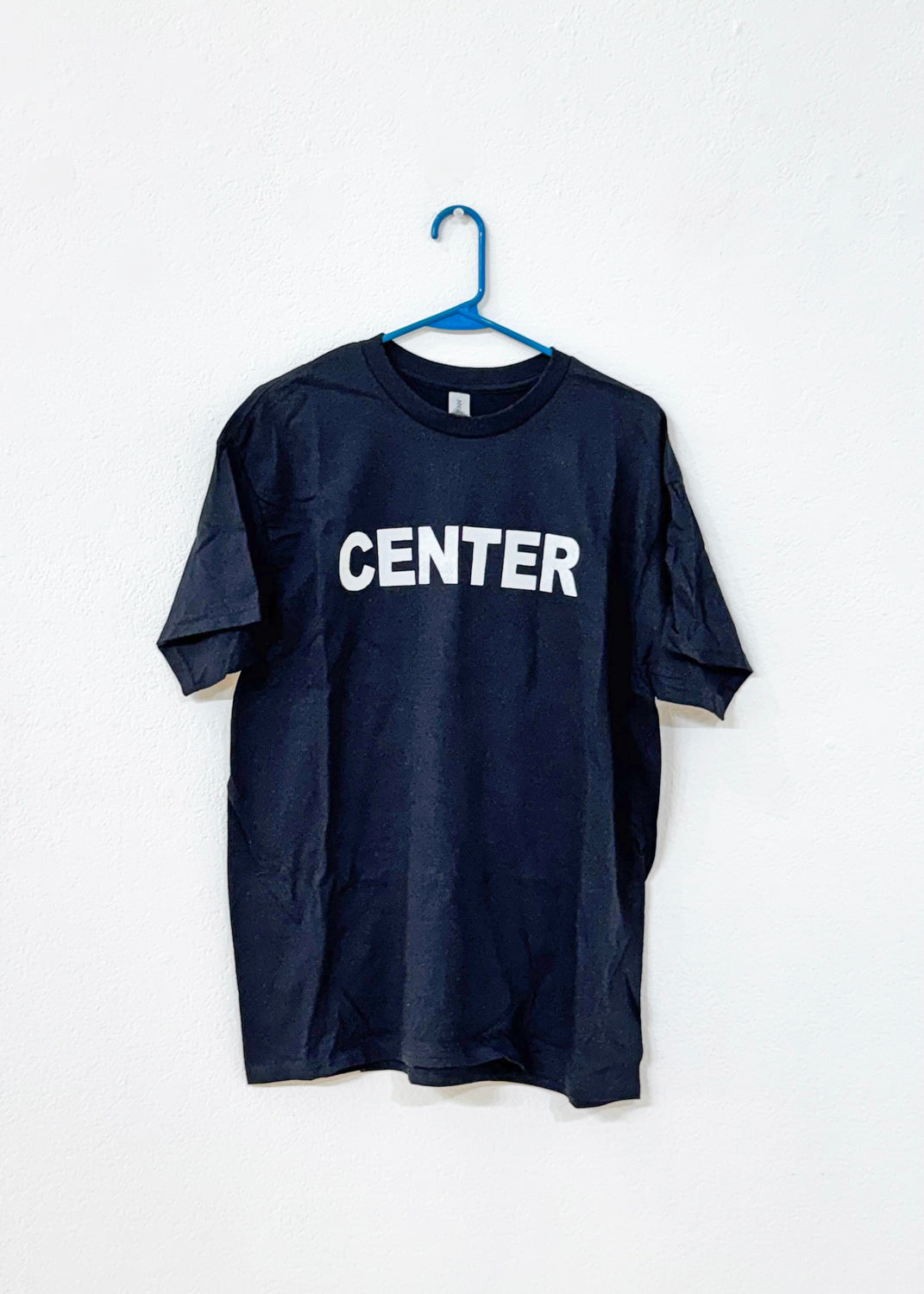 Black t-shirt with 'CENTER' printed on it, hanging on a white background, hanging from a blue hanger.