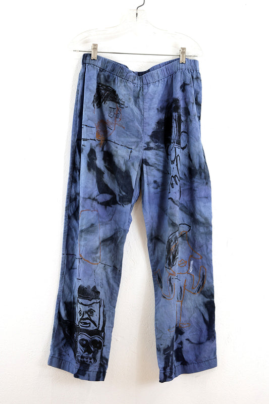 Light blue cotton pants with lighter blue  marks where the fabric was bleached by the sun and weather. The pants are illustrated with different faces across both legs with silkscreen prints in black and dark orange markers. 