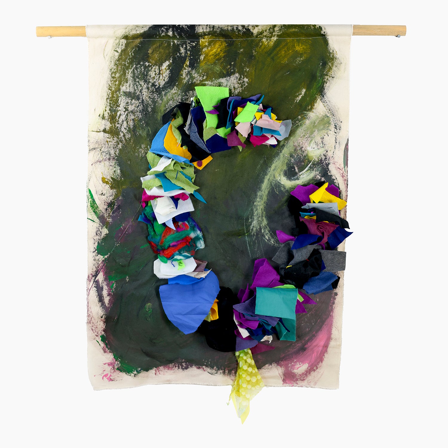 An abstract artwork on rectangular canvas hanging from a wooden rod. The background is predominantly painted in dark green with swirling abstract patterns, featuring subtle hints of black, white, and touches of pink. Across the central area is a prominent, irregularly shaped collage of vibrant, multicolored fabric pieces. These fabric scraps include bright blues, greens, purples, yellows, and reds, forming a visually striking contrast against the darker background.