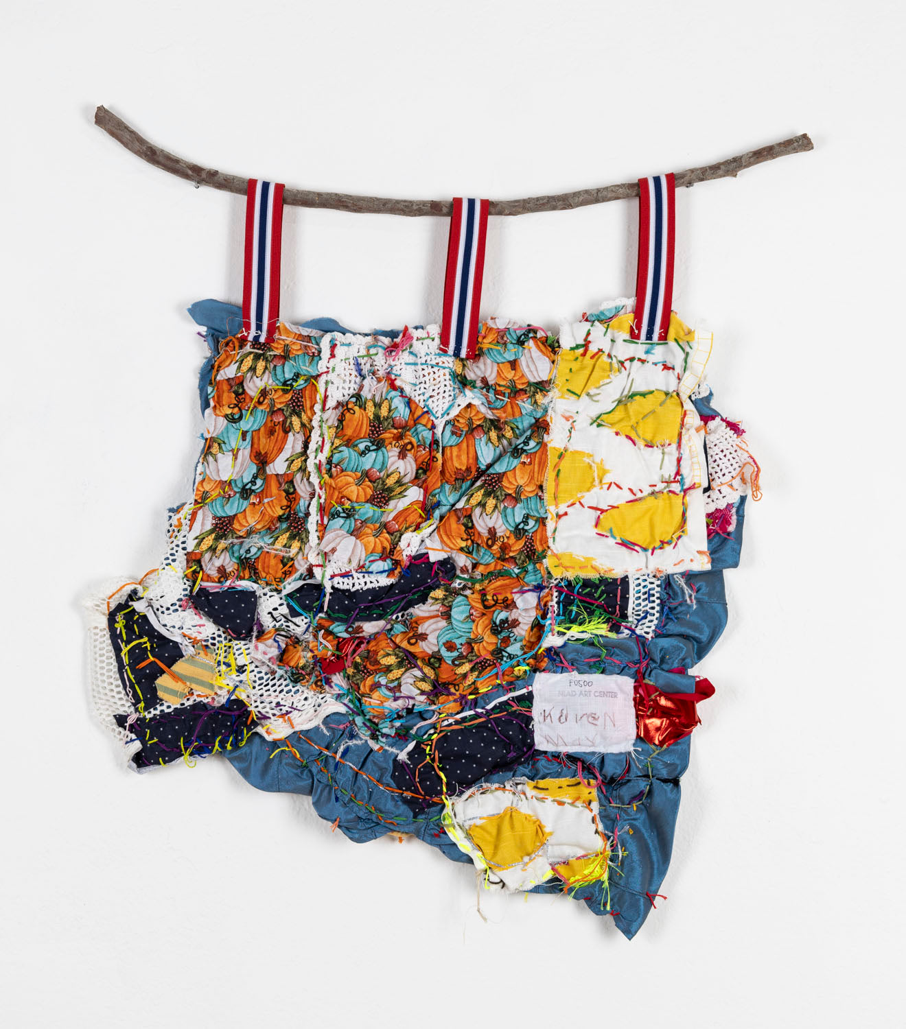 The same collage photographed from the back. There are fabrics printed with pumpkins and yellow spots covering most of the base blue cloth. The artist has signed the piece on a little swatch of white cotton, writing: Karen May