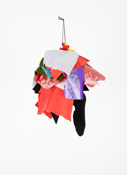 This fiber sculpture contains patches from different fabrics, arranged and sewn together. It is predominantly white, blue, red and black.