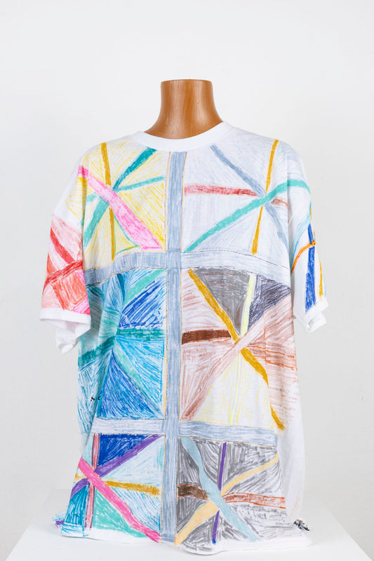 A wooden mannequin torso wearing a white teeshirt. Using fabric markers, the artist has covered the shirt with hand drawn geometric patterns, mostly shaped like asterisks with each segment colored a different shade of yellow, blue, grey, or pink. 