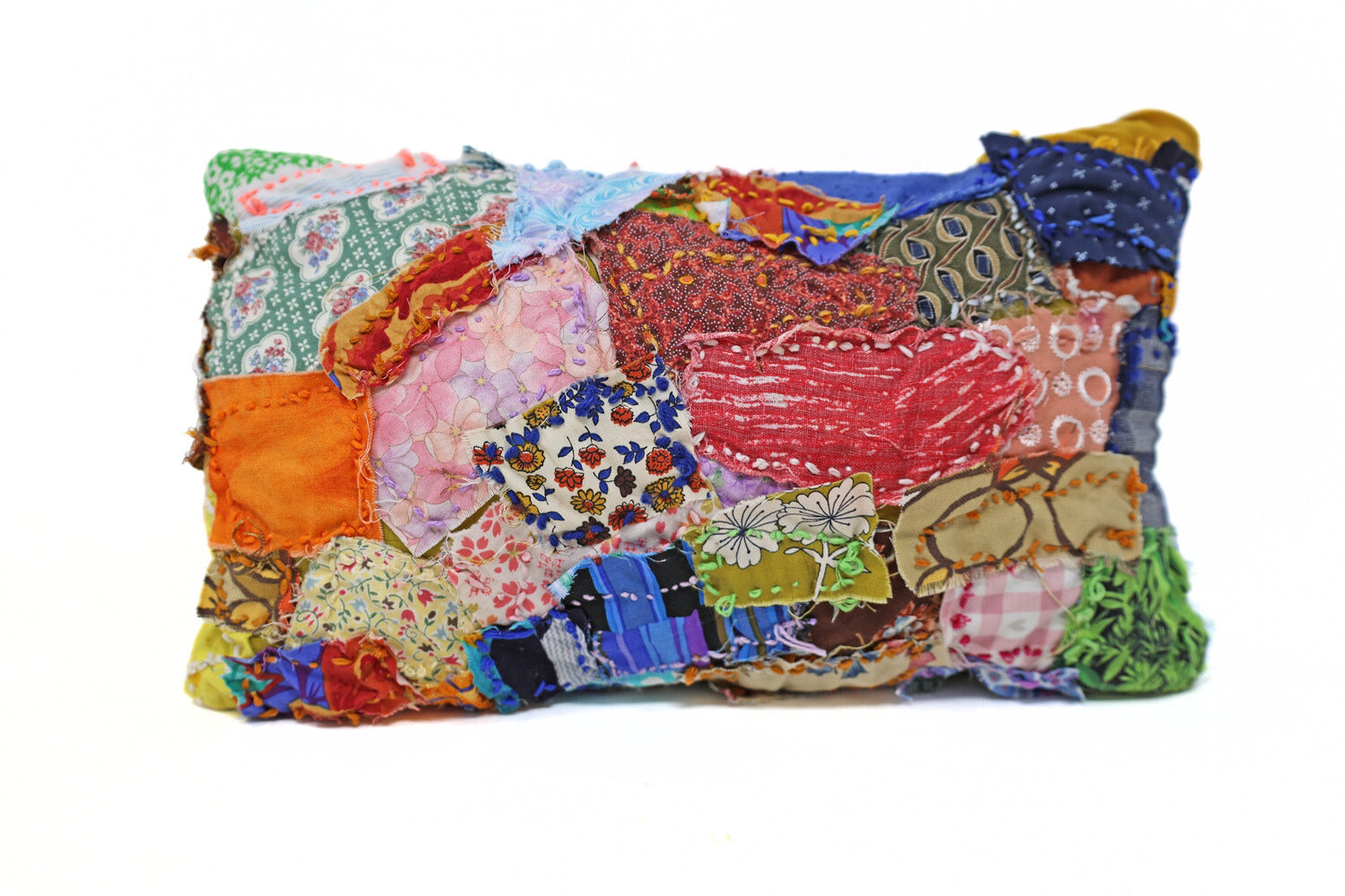 This fiber pillow incorporates various patterns and materials to form a patchwork style. It has vibrant colors and patterns, with many of the fabrics containing floral elements. There are also embroidered details.