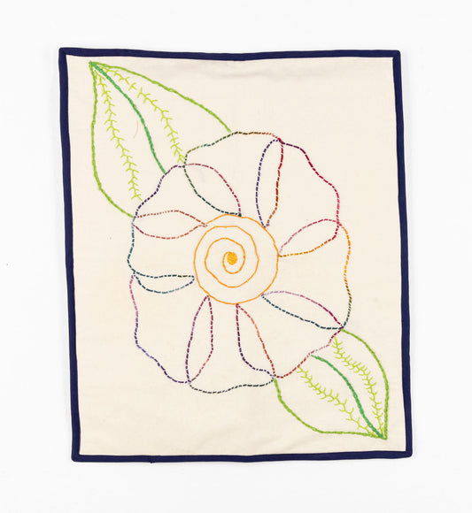 This fiber piece has a large flower embroidered onto fabric. The middle of the flower is a vibrant yellow thread, with blue, pink and purple petals. The leaves are varying shades of green. The flower is depicted through a strong sense of line-work against the beige background. 