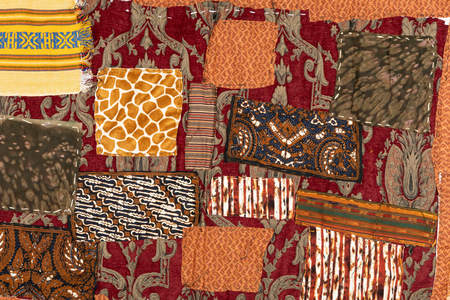 This is a fiber piece hanging on a wooden dowel. The base fabric is orange with a brown floral pattern. On top there are patches with different patterns that are layered and embroidered on with white thread.