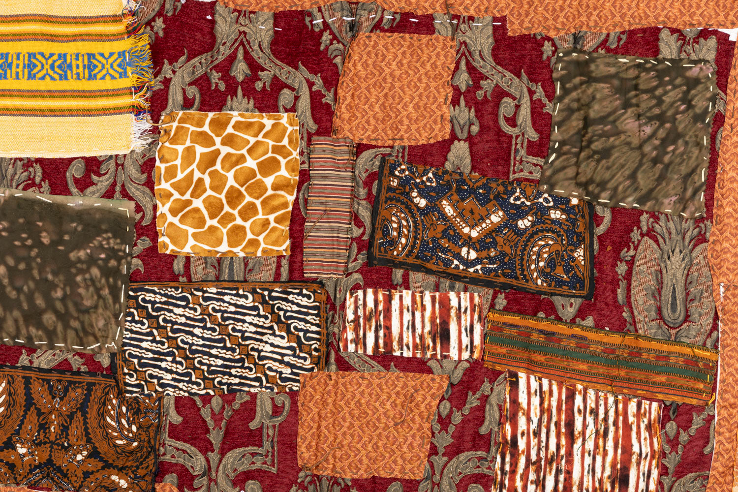 This is a fiber piece hanging on a wooden dowel. The base fabric is orange with a brown floral pattern. On top there are patches with different patterns that are layered and embroidered on with white thread.