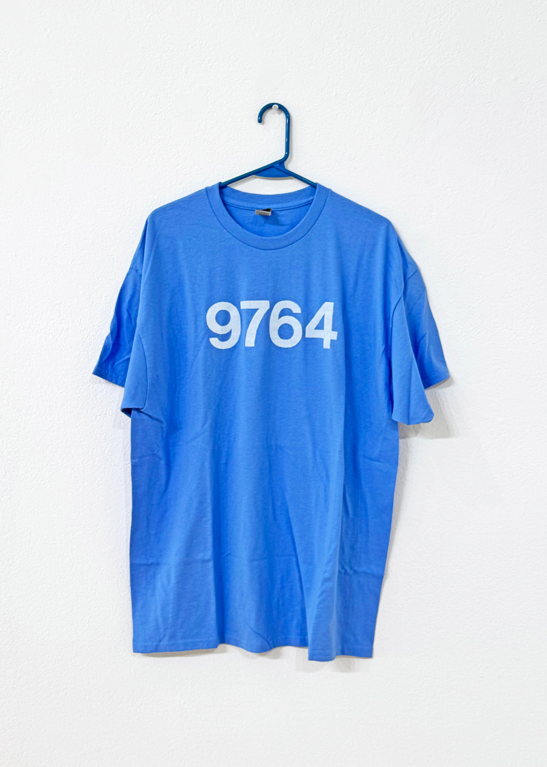 Blue t-shirt with '9764' printed on it hanging on a white background, hanging on a blue hanger