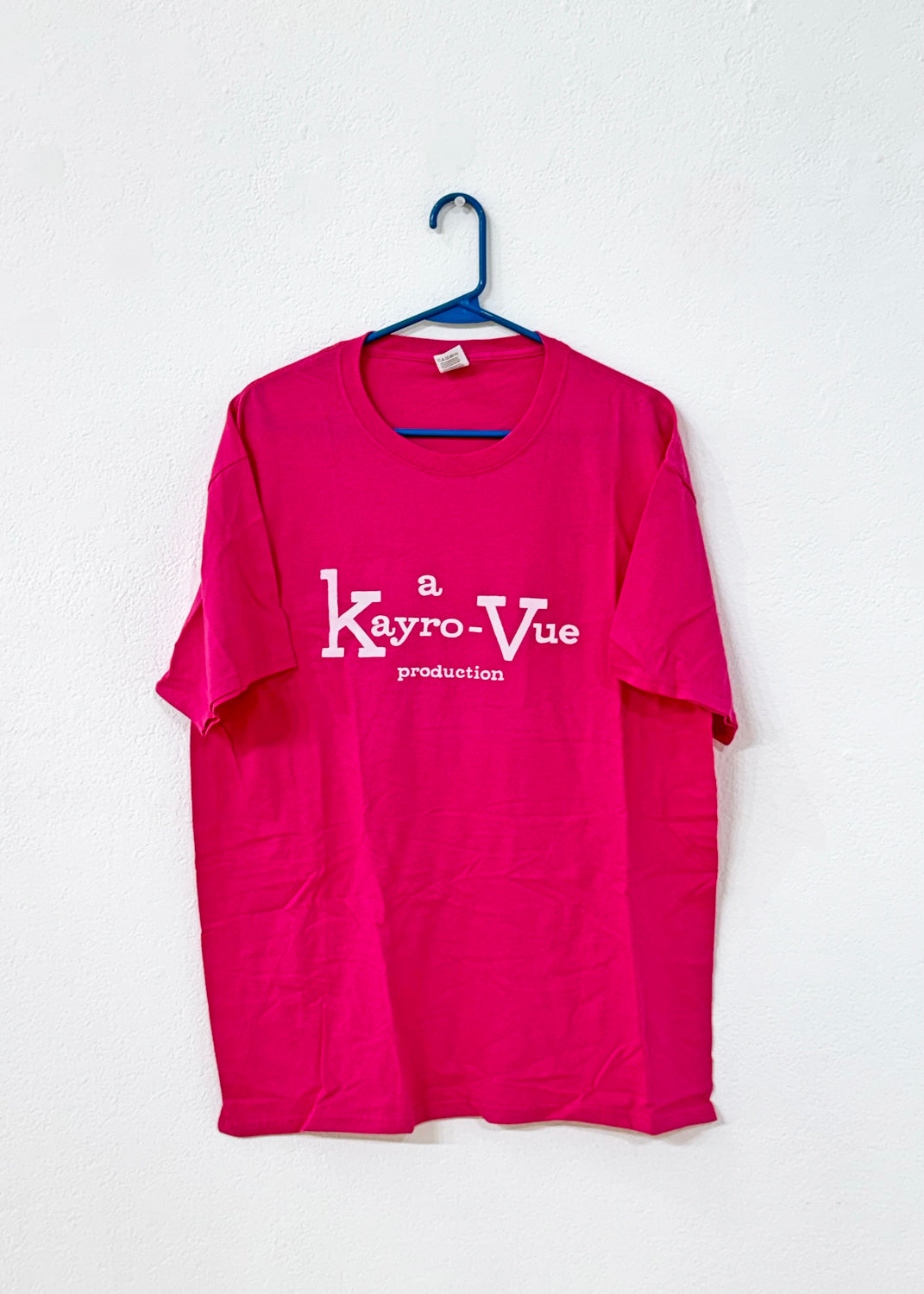 Pink t-shirt with 'a Kayro-Vue production' text on a white background, having on a blue hanger