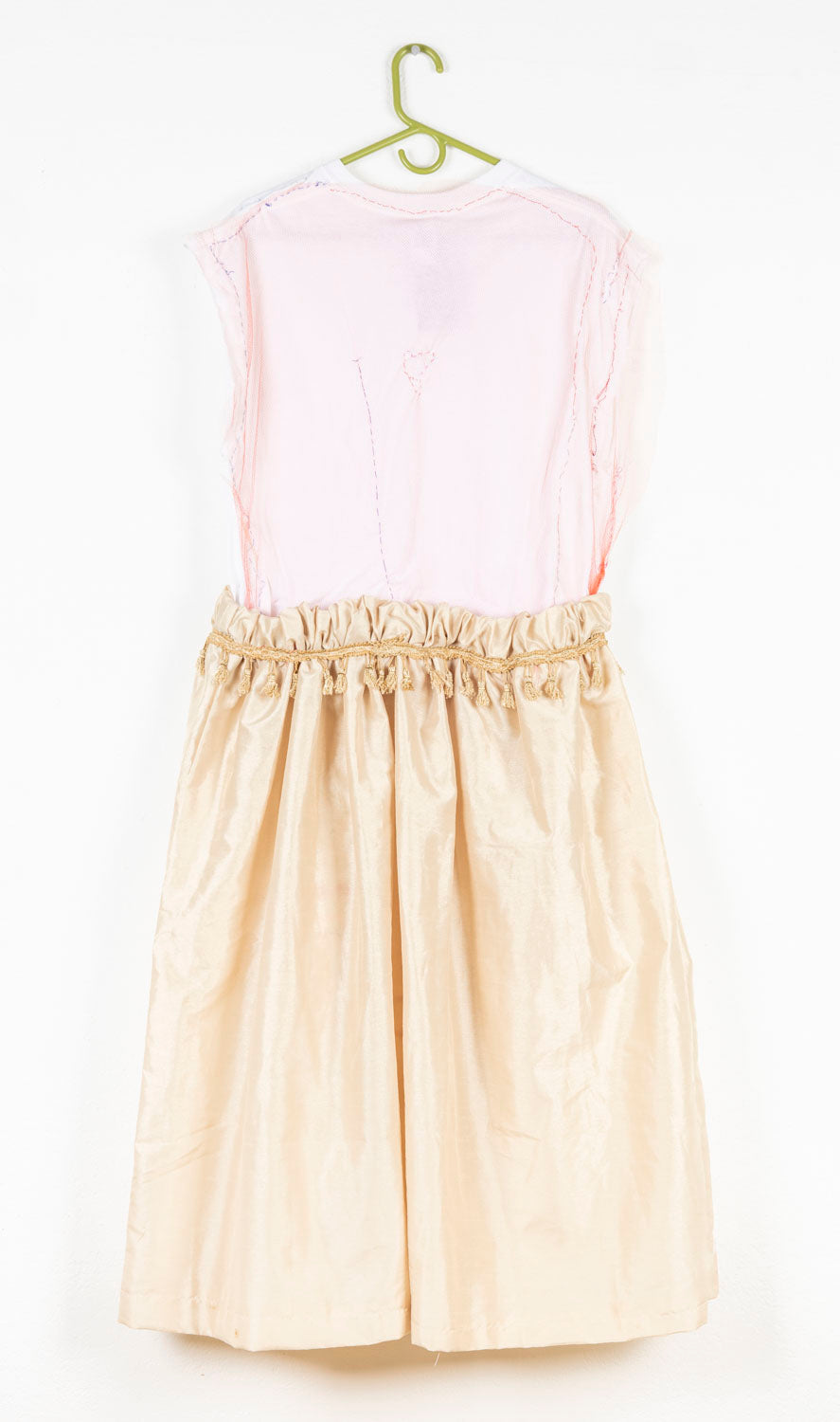 This wearable garment has a white top sewn onto a gold skirt. The waist of the garment is cinched with gold tassels. There is an embroidered heart on the back of the piece.