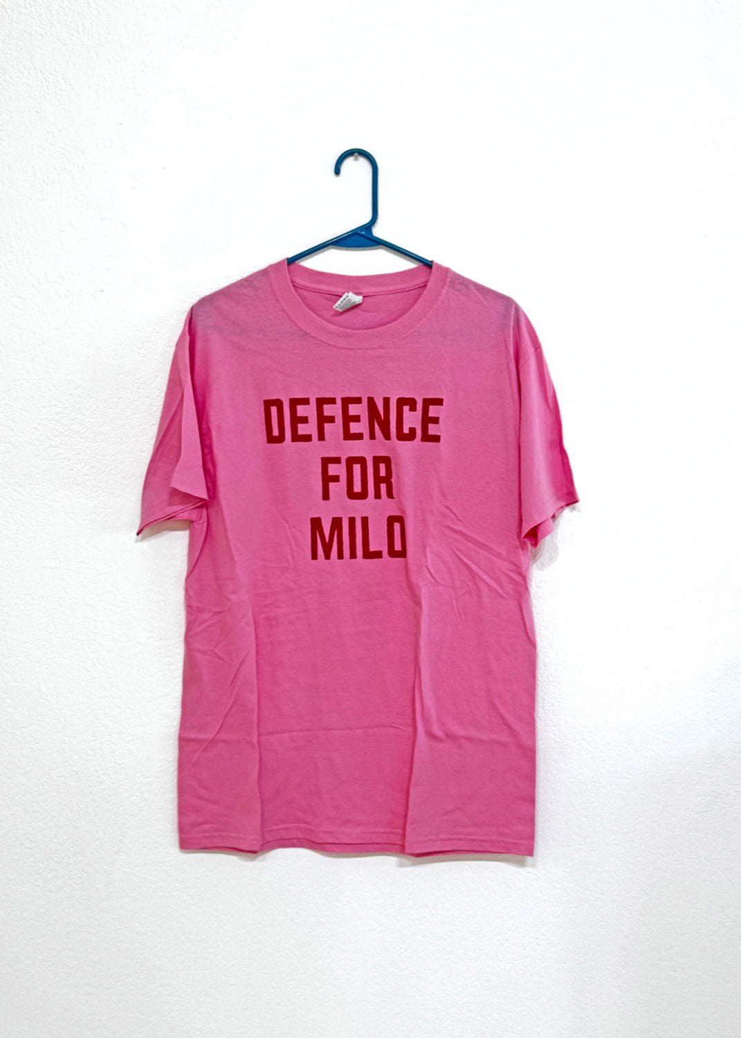 A bright pink T-shirt with the text 'Defence For Milo' screen printed onto the front with a red ink.
