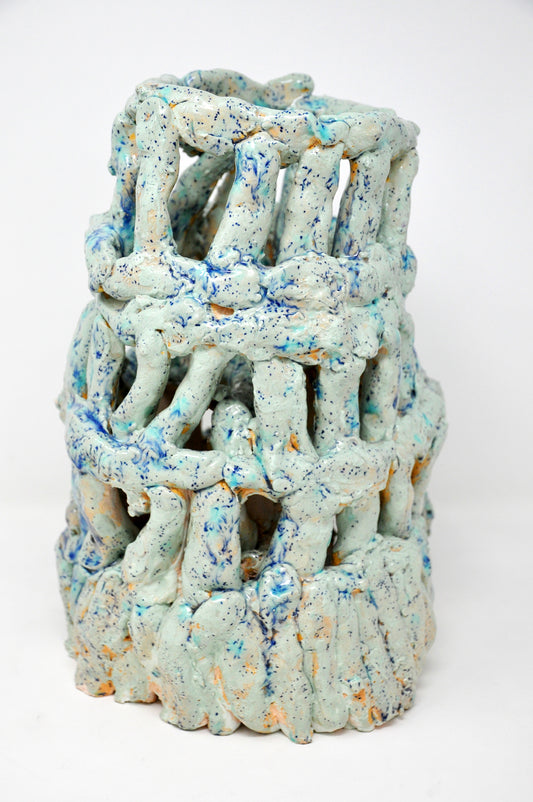 A ceramic sculpture of a tower. It's coated with glossy teal glaze speckled all over with bright royal blue spots. The tower is four tiers tall, wider at the base. It's made of little cylinders: some are stacked vertically and others are wrapped around the tower in horizontal bands. There are gaps between each cylinder through which the white background or dark interior are visible.