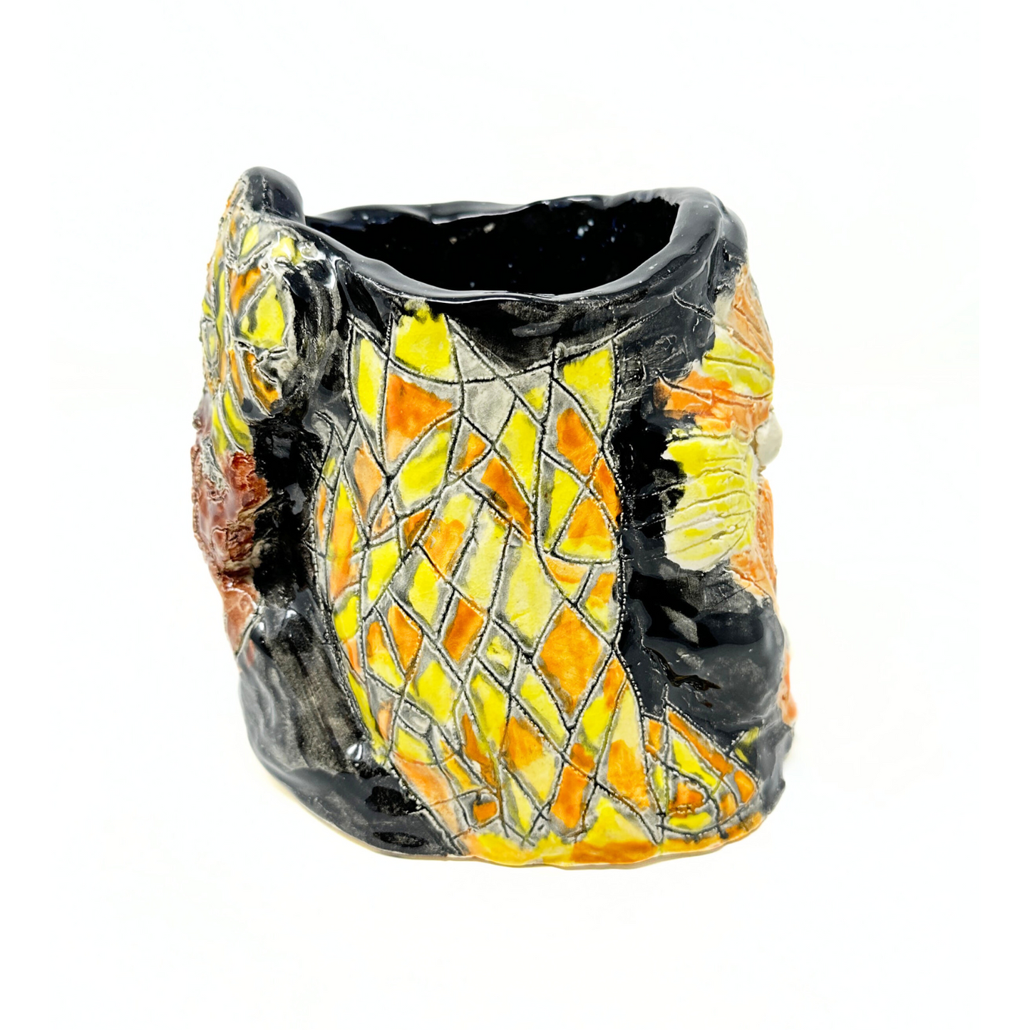 The same ceramic vessel photographed from the side. From this angle the opening of the vessel is in view, showing that the interior is glazed dark shiny black. The exterior of the side of the vessel has an abstract diamond pattern etched onto the surface, glazed yellow orange and grey. 