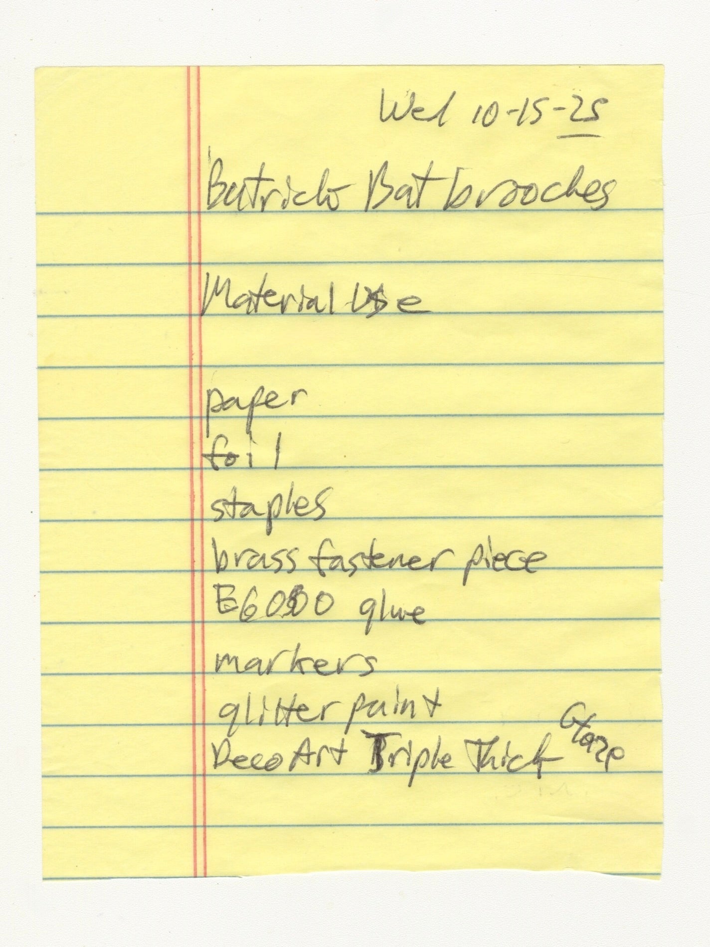 A handwritten note on yellow lined paper. The note includes a list of materials used to construct the brooch, including: Paper, foil, staples, brass fastener piece, glue, markers, glitter paint, and deco art triple thick glaze.