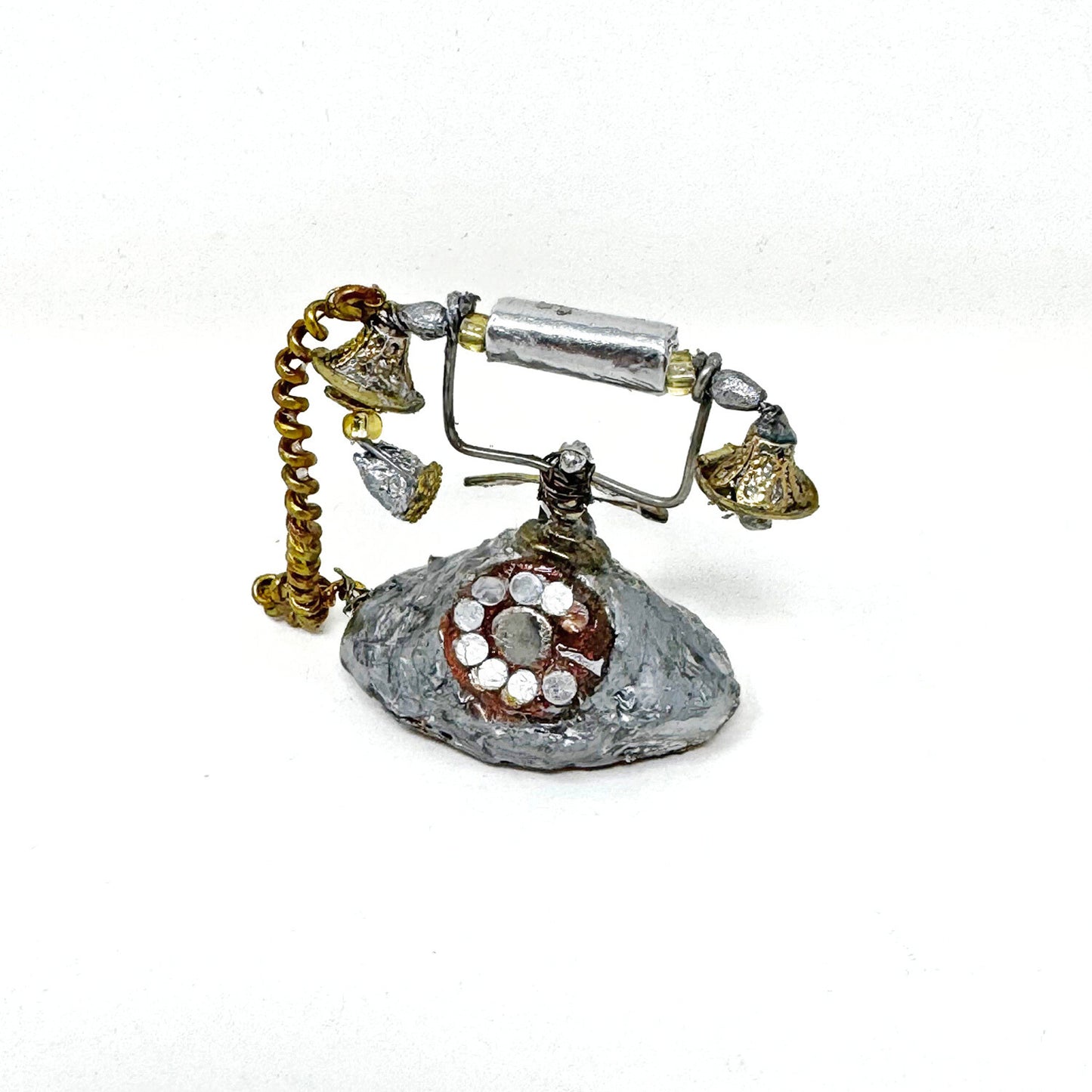 A mini sculpture of a silver antique style rotary phone, made of recycled materials against a white background.