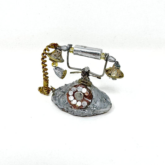 A mini sculpture of a silver antique style rotary phone, made of recycled materials against a white background.