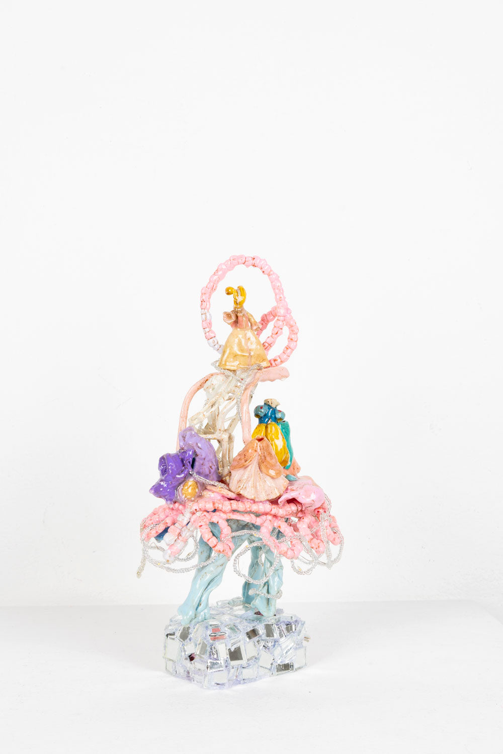 A plastic assemblage sculpture made out of melted toys with mirror mosaic base. A surreal princess ball scene on top of a powder blue running horse body. Fairy lights illuminated and strung throughout the piece.