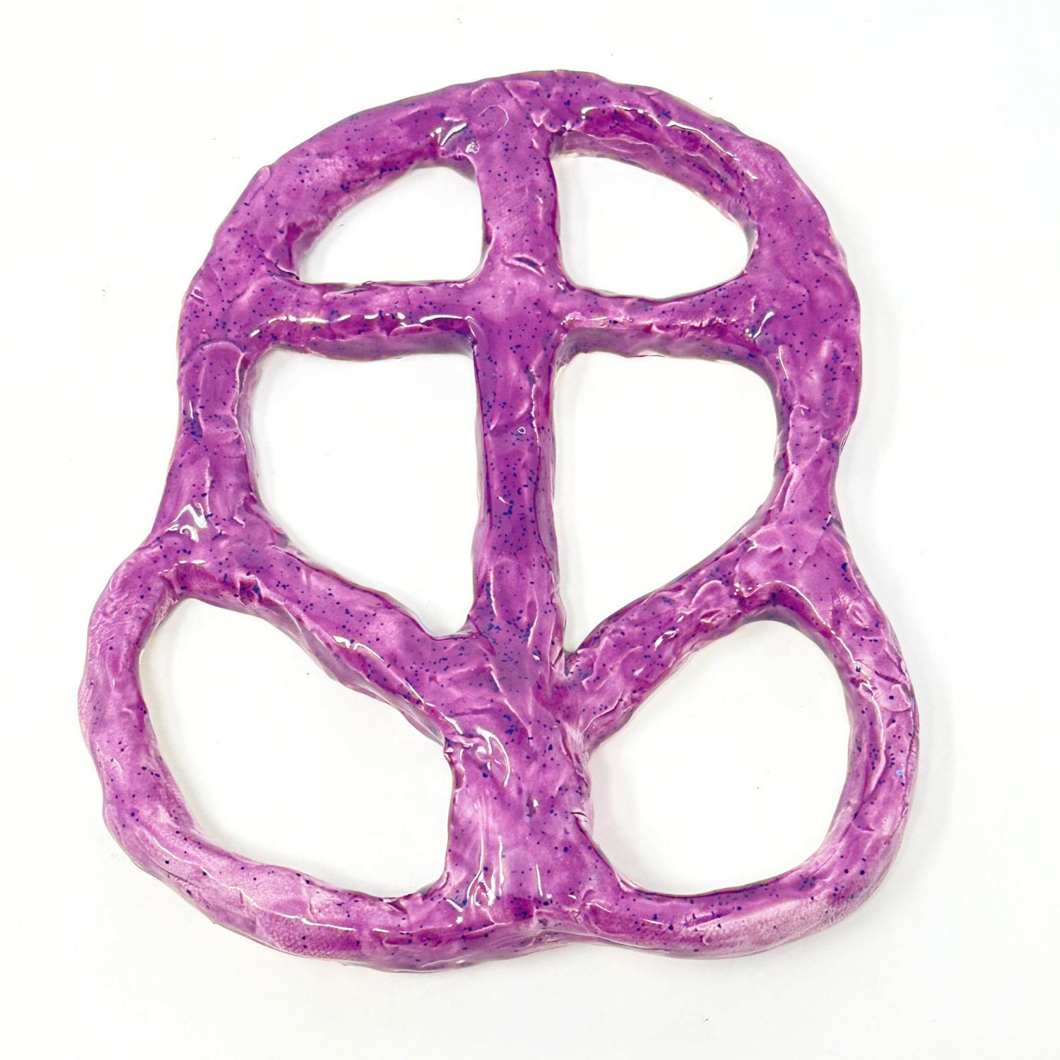 an abstract ceramic sculpture glazed all over in bright purple speckled with blue dots. The shape is a symbol made of coils of clay. The outer edge forms an oval and the interior is bisected by interlocking tubes, similar to how iron work divides shaped panes in a stained glass window. 